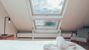 Ein Schlafzimmer mit Oberlicht, einem Bett, einem Sessel und einem Nachttisch.