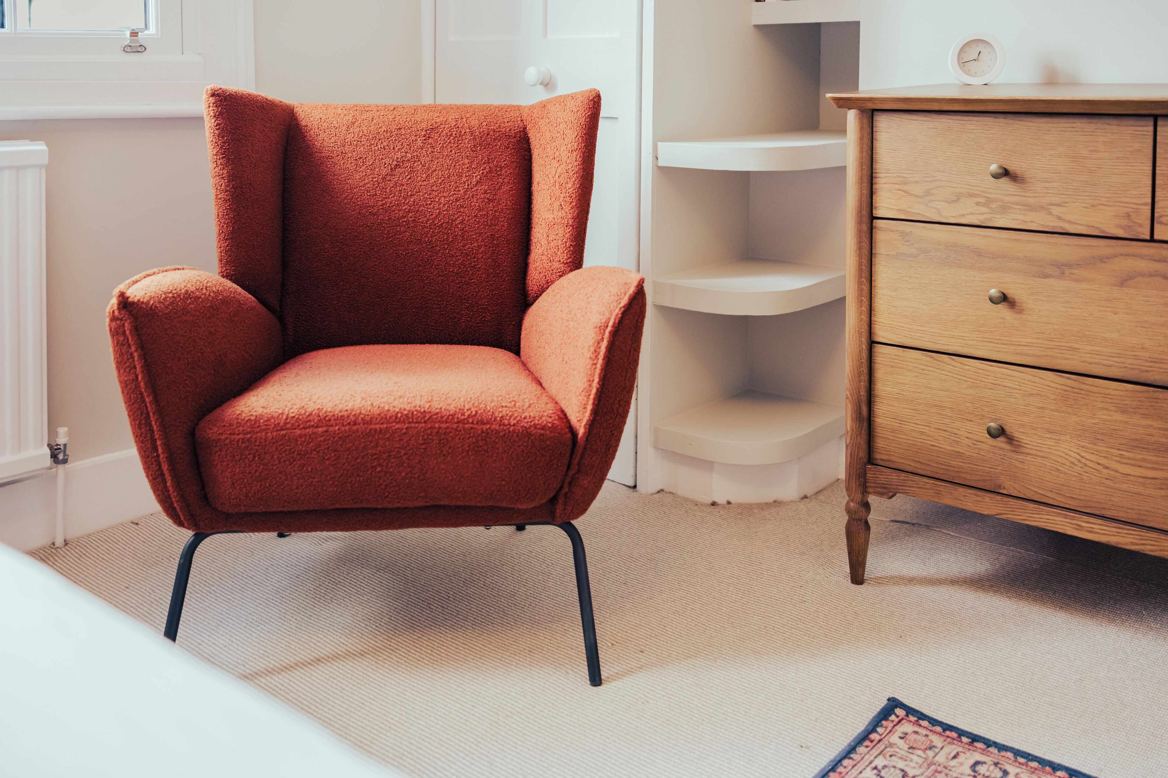 A room with a red armchair, a wooden dresser, and a white radiator.