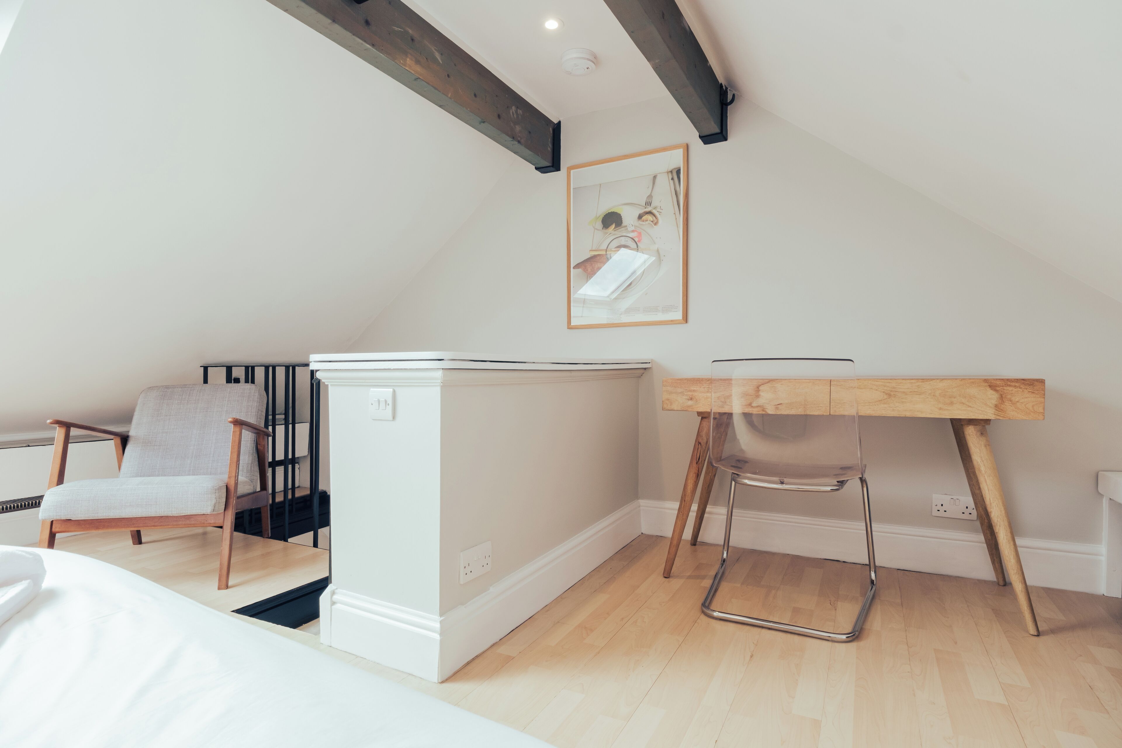 A small, modern bedroom with a loft-style ceiling, a wooden desk, a chair, a bed, and a radiator.
