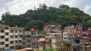 A densely packed urban area with multi-story buildings, some with balconies and terraces, surrounded by lush green hills.