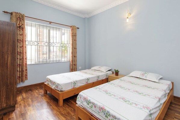 Une pièce avec deux lits en bois, une fenêtre avec des rideaux et un luminaire fixé au mur.