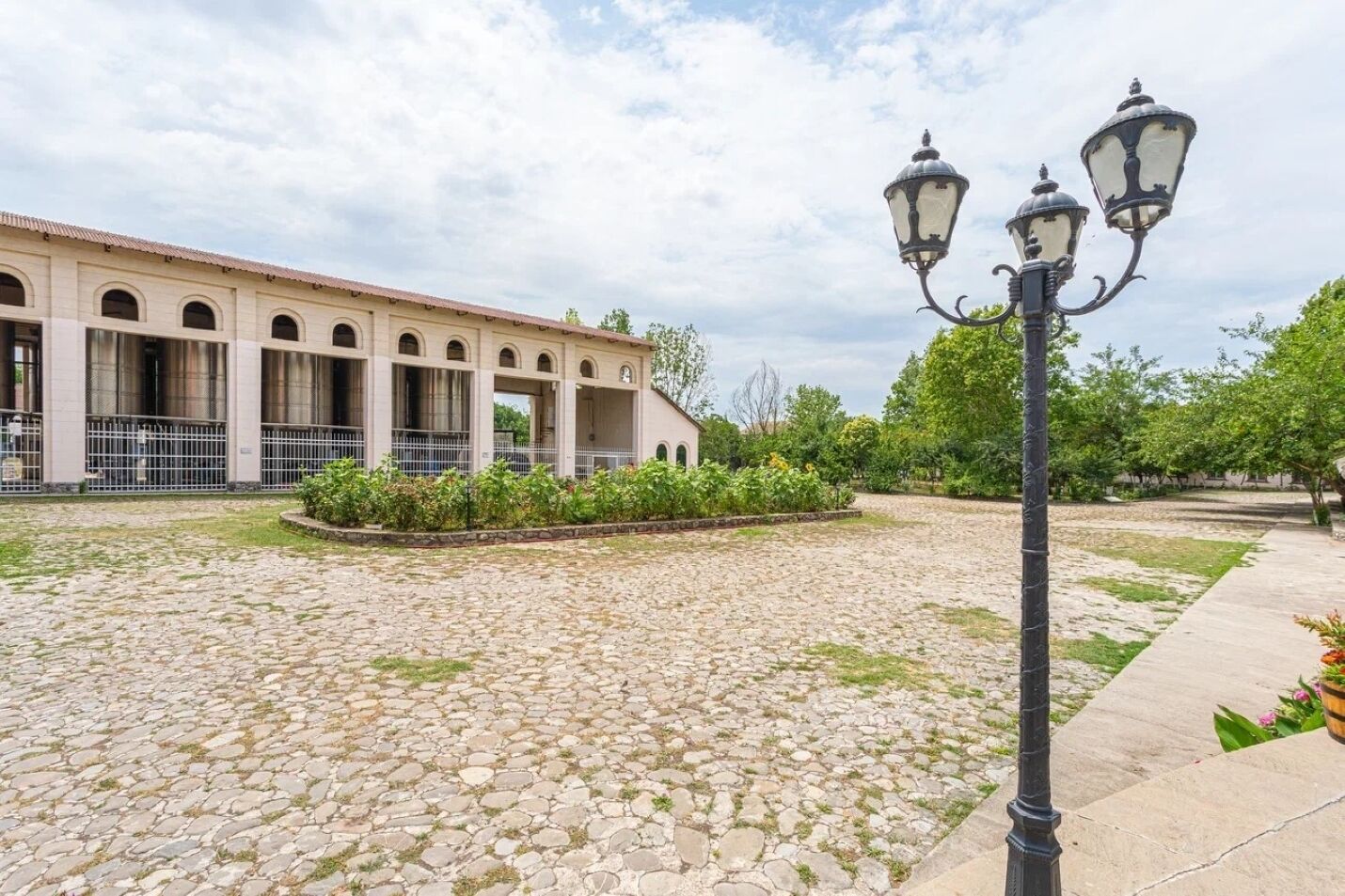 A courtyard with cobblestone flooring, a building with arched windows, and a street lamp.
