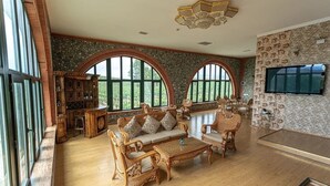 A spacious living room with a large arched window, wooden furniture, a stone wall, and a mounted TV. - Winery Chabiant Hotel (Ismailli)
