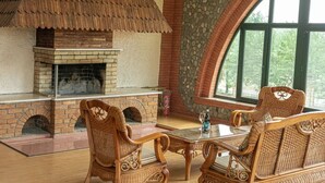 A cozy room with a brick fireplace, wicker furniture, and large windows. - Winery Chabiant Hotel (Ismailli)