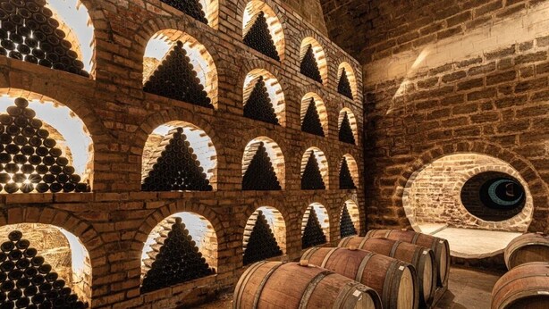A wine cellar with wooden barrels and bottles arranged in arched niches. - Winery Chabiant Hotel (Ismailli)