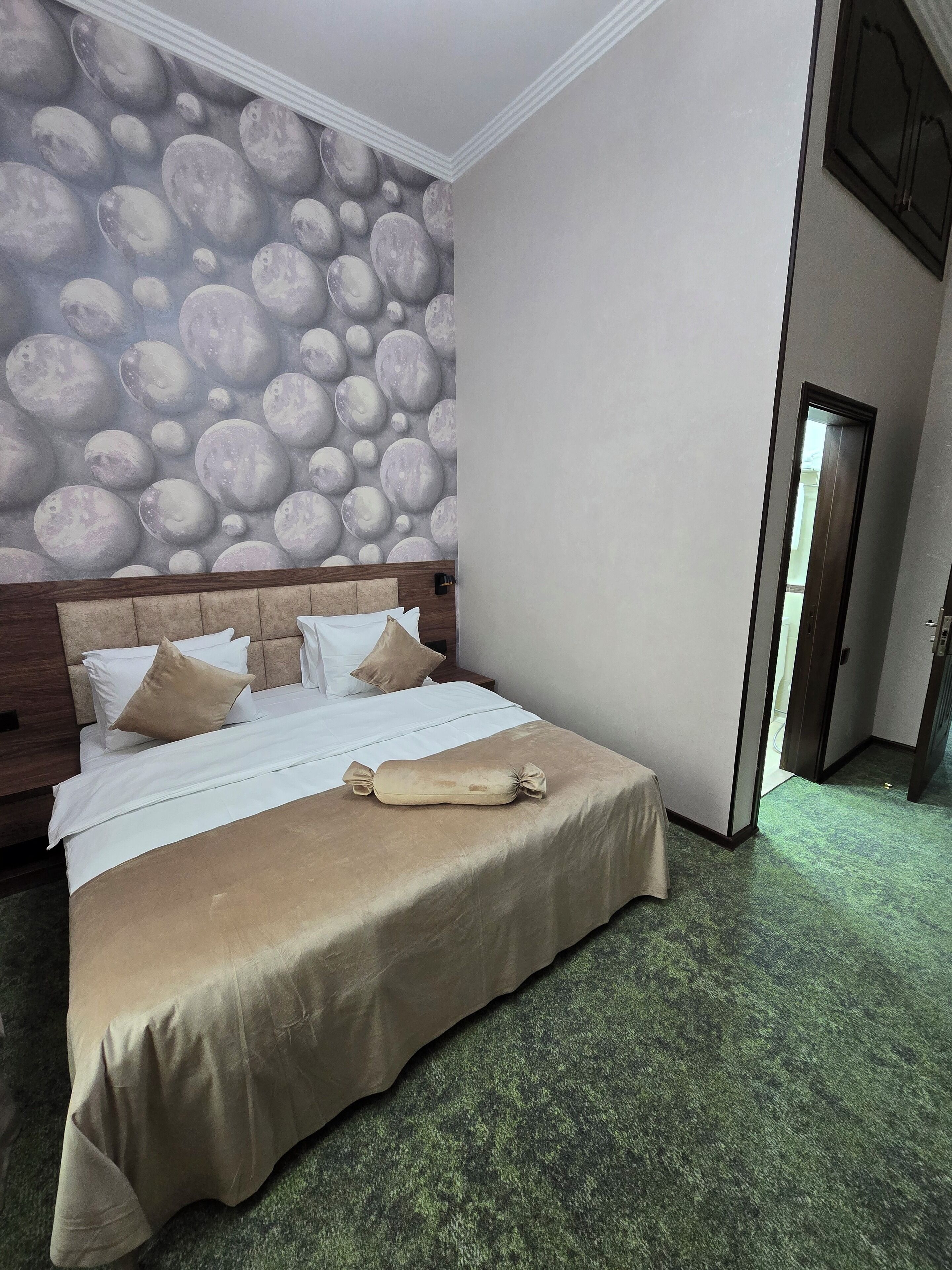 Habitación de hotel con cama, cabecera, un suelo alfombrado y un mural celeste en la pared.