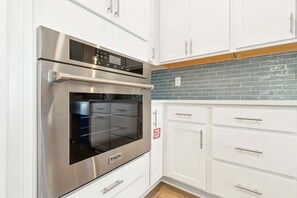 Una cocina con armarios blancos, un horno de acero inoxidable y un salpicadero de azulejos azules.