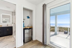 Eine moderne Küche mit dunklen Schränken, einem Edelstahlkühlschrank und Blick auf den Strand durch eine große Glasschiebetür.