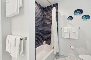 Un baño con una bañera, un cortinón de ducha y tres toallas colgadas en la pared.