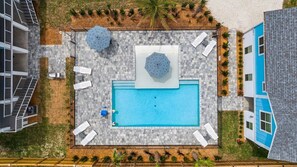 Vista aérea de un hotel moderno con piscina rectangular, mobiliario exterior y jardín ajardinado.