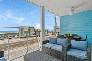 Un balcón con mobiliario de mimbre, ventilador de techo y vista a la playa y edificios.