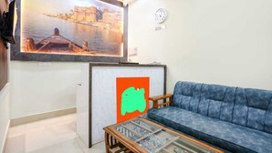 A living room with a blue sofa, a glass coffee table, a framed picture of a river scene, and a wall clock. - Aditya GH (Varanasi)