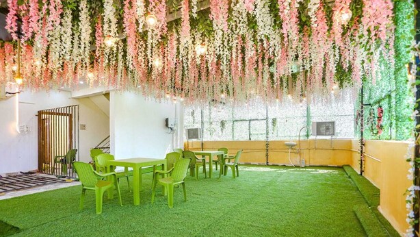 A room with artificial grass flooring, green plastic chairs, and tables. - Aditya GH (Varanasi)