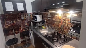Une cuisine avec des meubles de couleur sombre, un four à micro-ondes, une cuisinière et un évier. On y trouve également deux tabourets de bar et un lave-linge.