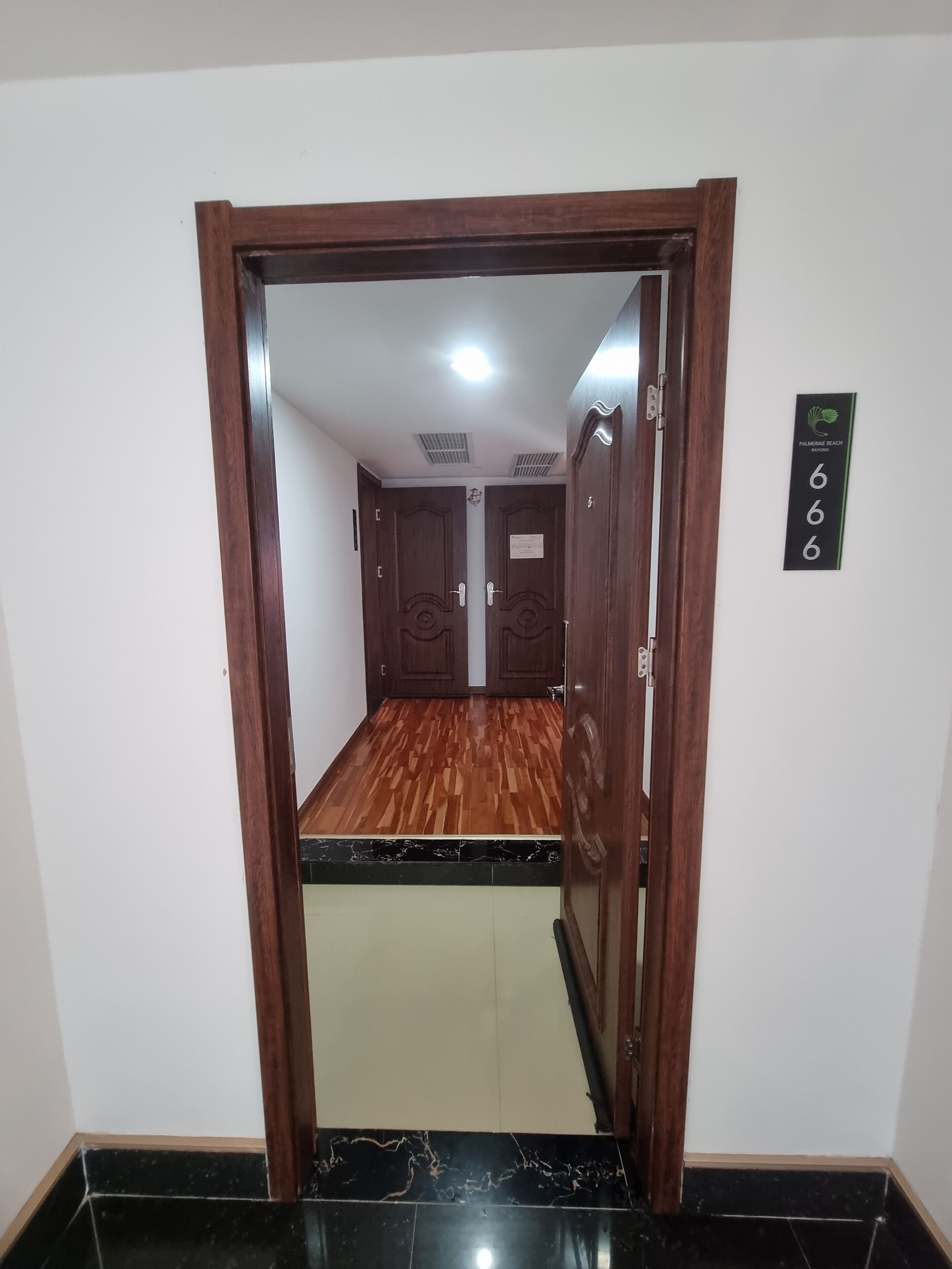 Entrada de hotel con marco de madera, letrero con número y vista a una habitación con piso estampado y puerta con diseño decorativo.