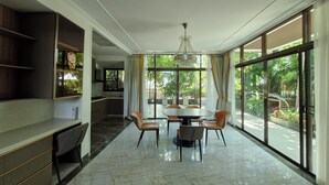 A spacious dining area with a large table and chairs, a kitchen in the background, and large windows offering a view of greenery. - Palmeraiebeach Resort Rayong (Klaeng)