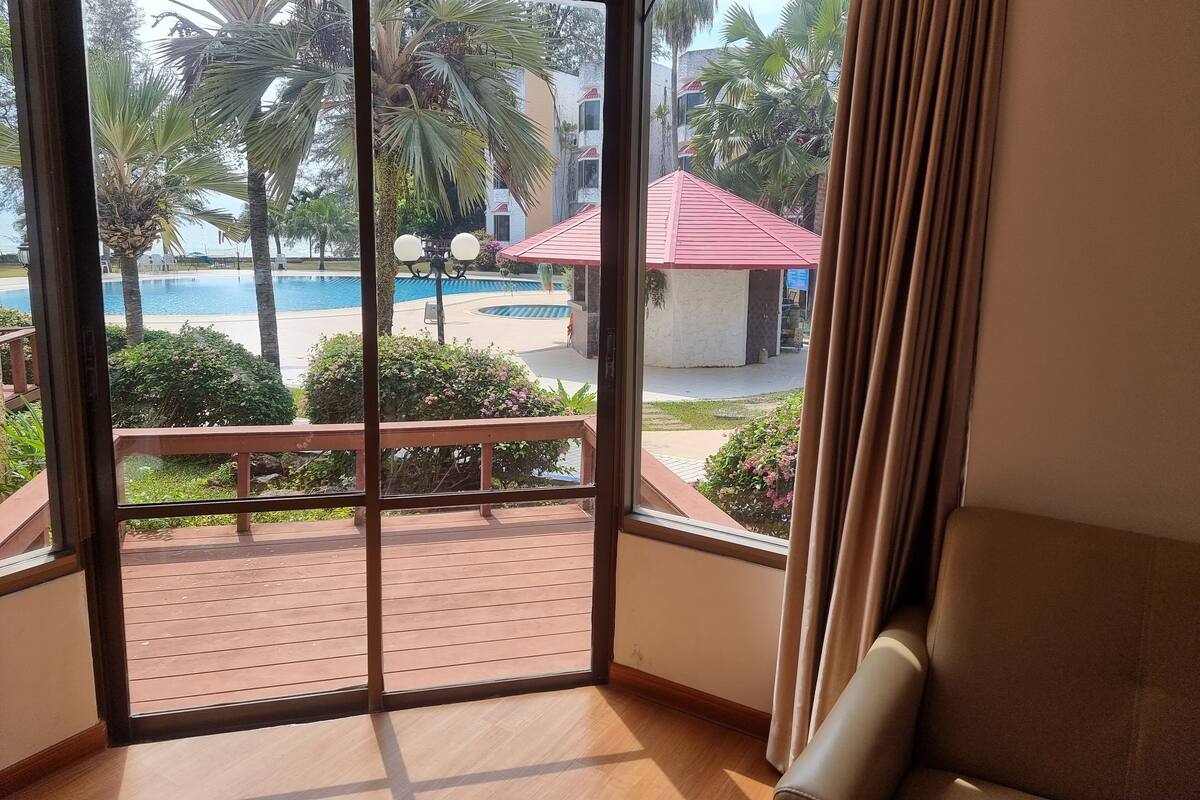 A room with a large sliding glass door leading to a pool area, a wooden deck, and a view of a building with a red roof.