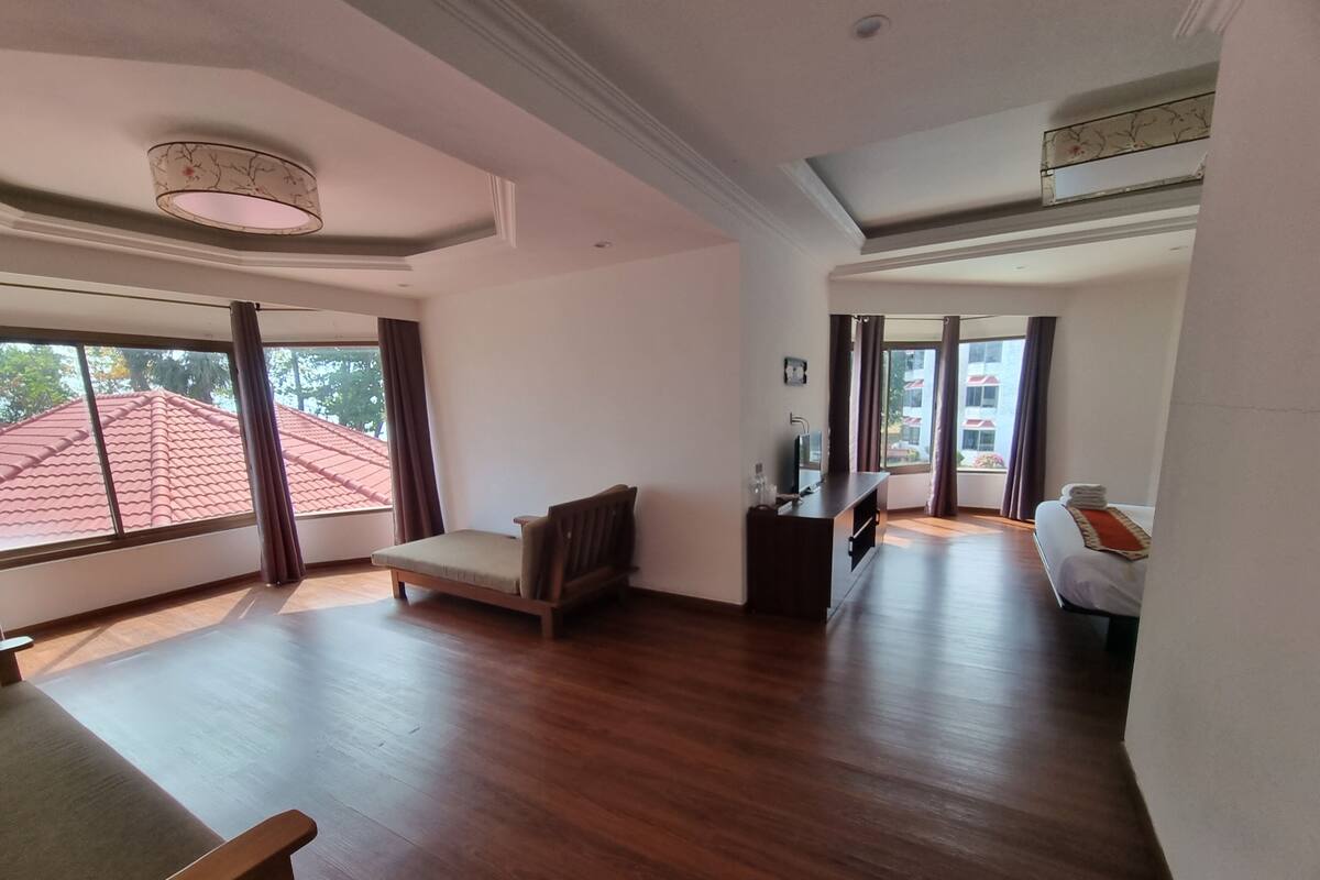 A spacious room with a wooden floor, a small sofa, a desk with a chair, and a bed with a red blanket.