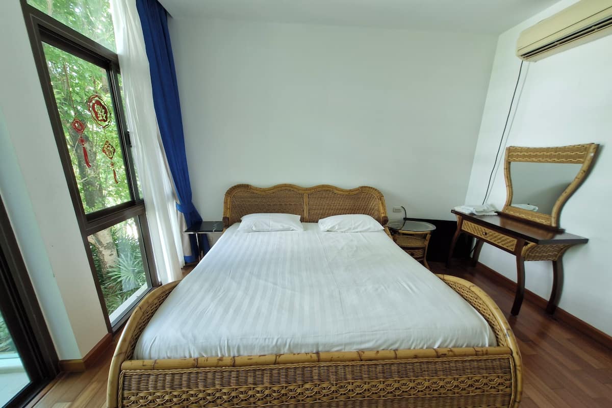 A neatly made bed with a woven headboard, a bedside table, a chair, and a mirror on the wall.