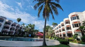 A hotel with a pool, palm trees, and a clear blue sky. - Palmeraiebeach Resort Rayong (Klaeng)