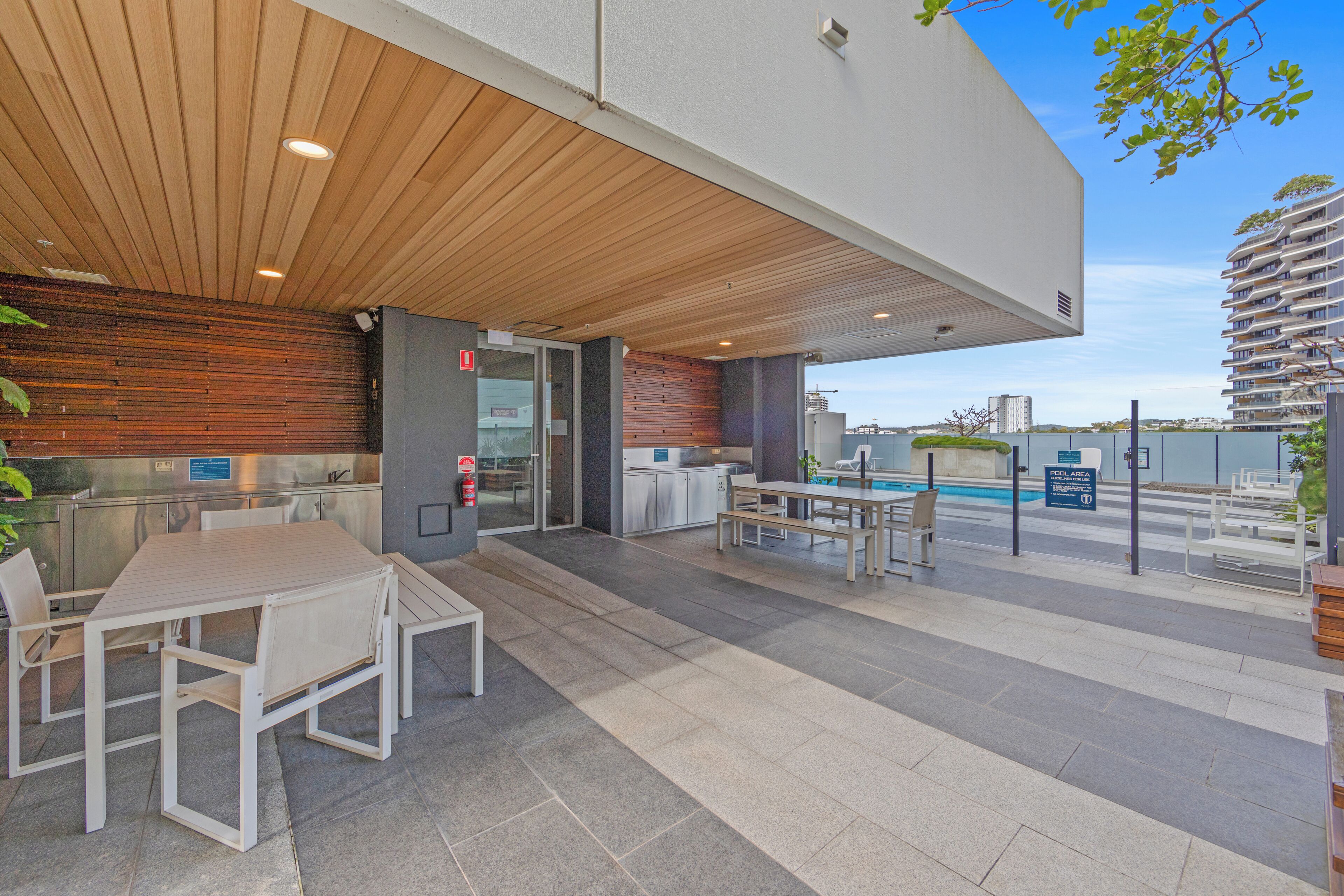 Un área de comedor al aire libre con vista a la piscina, techo de madera y diseño moderno.