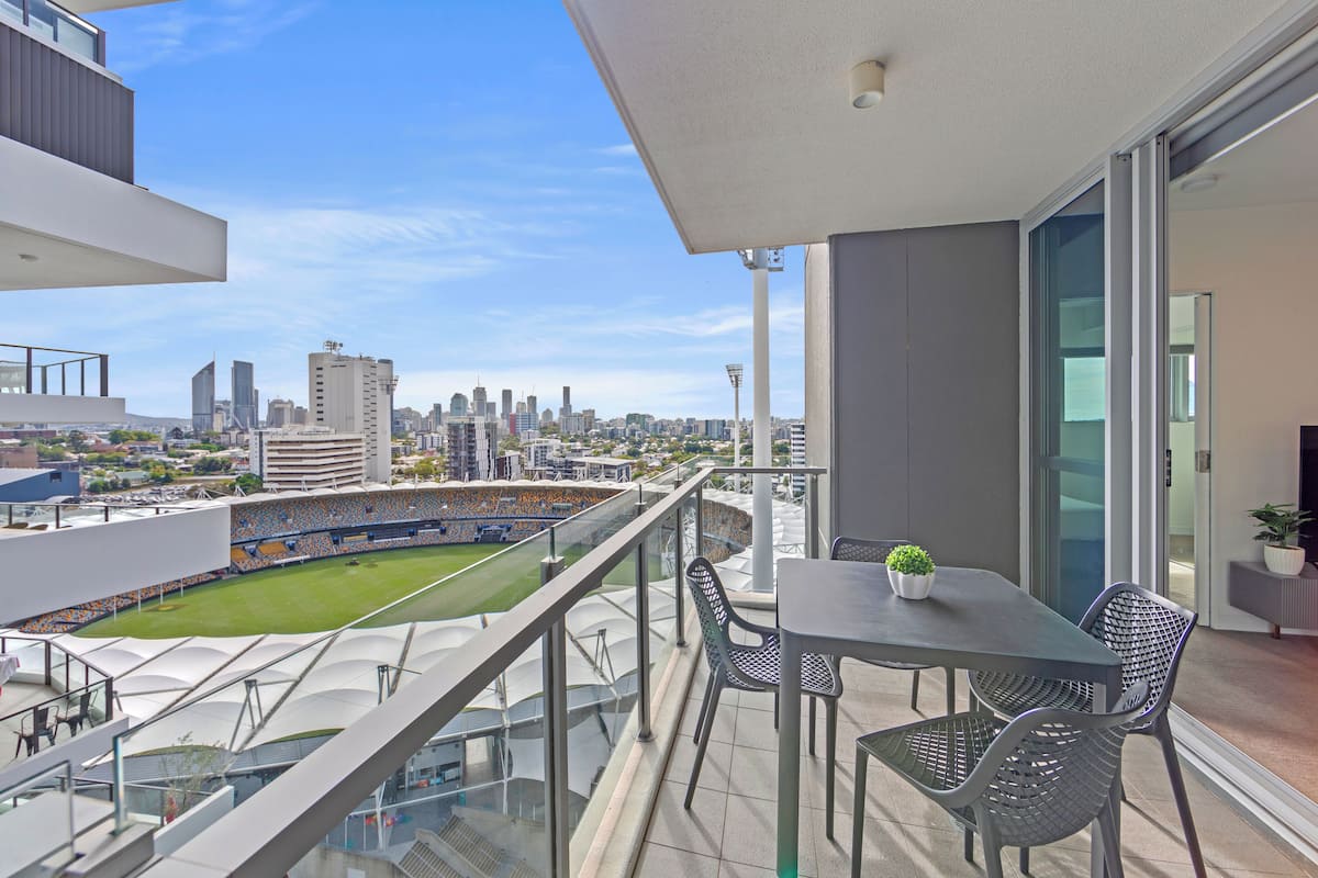A balcony with a table and chairs, overlooking a stadium and city skyline.