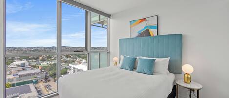 A modern hotel room with a large bed, a view of the city, and a blue headboard.