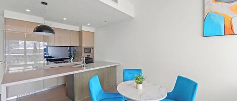 Una cocina moderna con una isla central, sillas azules y una mesa de mármol blanco.