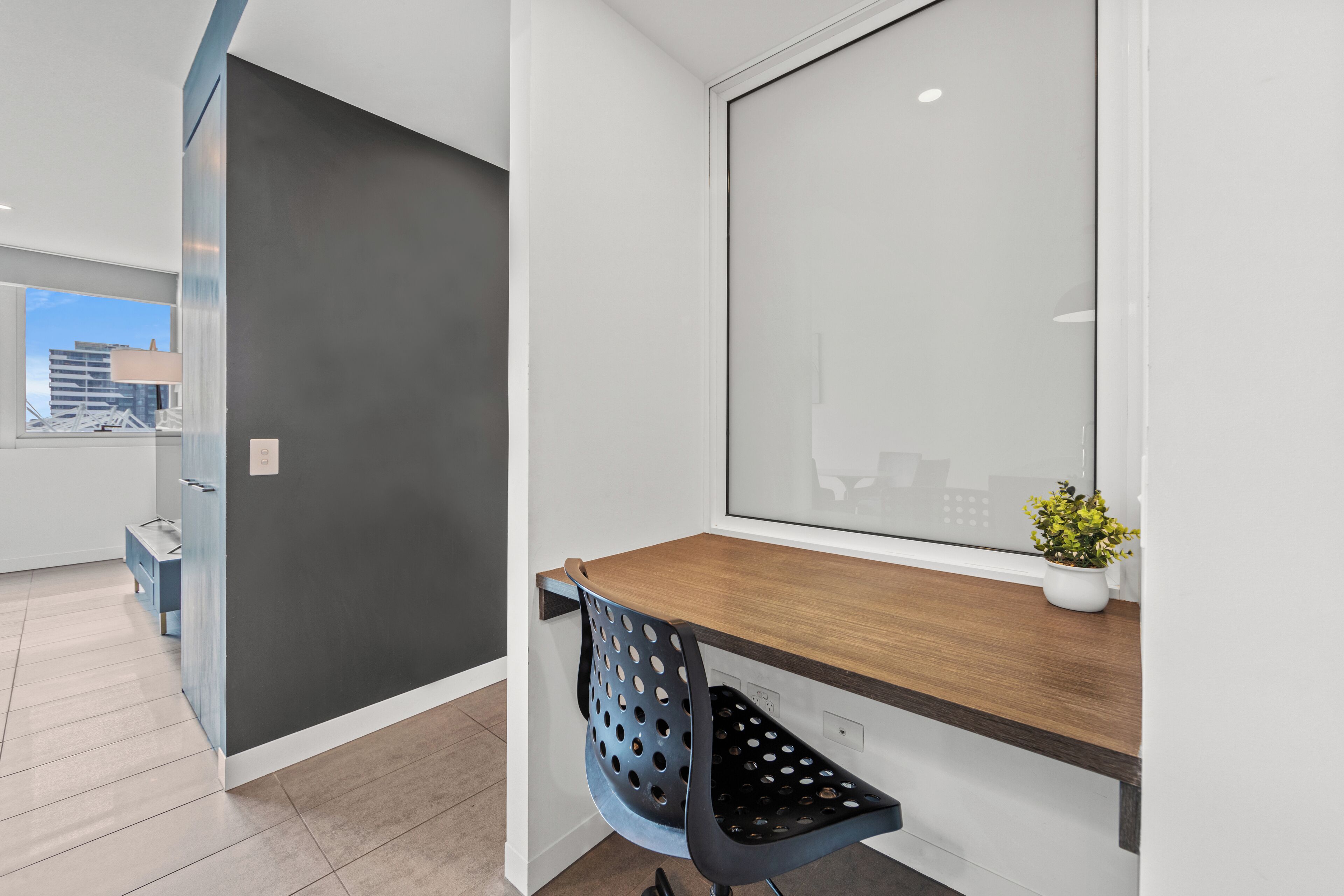 Un espacio de oficina moderno con una pared gris oscuro, un escritorio de madera y una silla azul perforada.