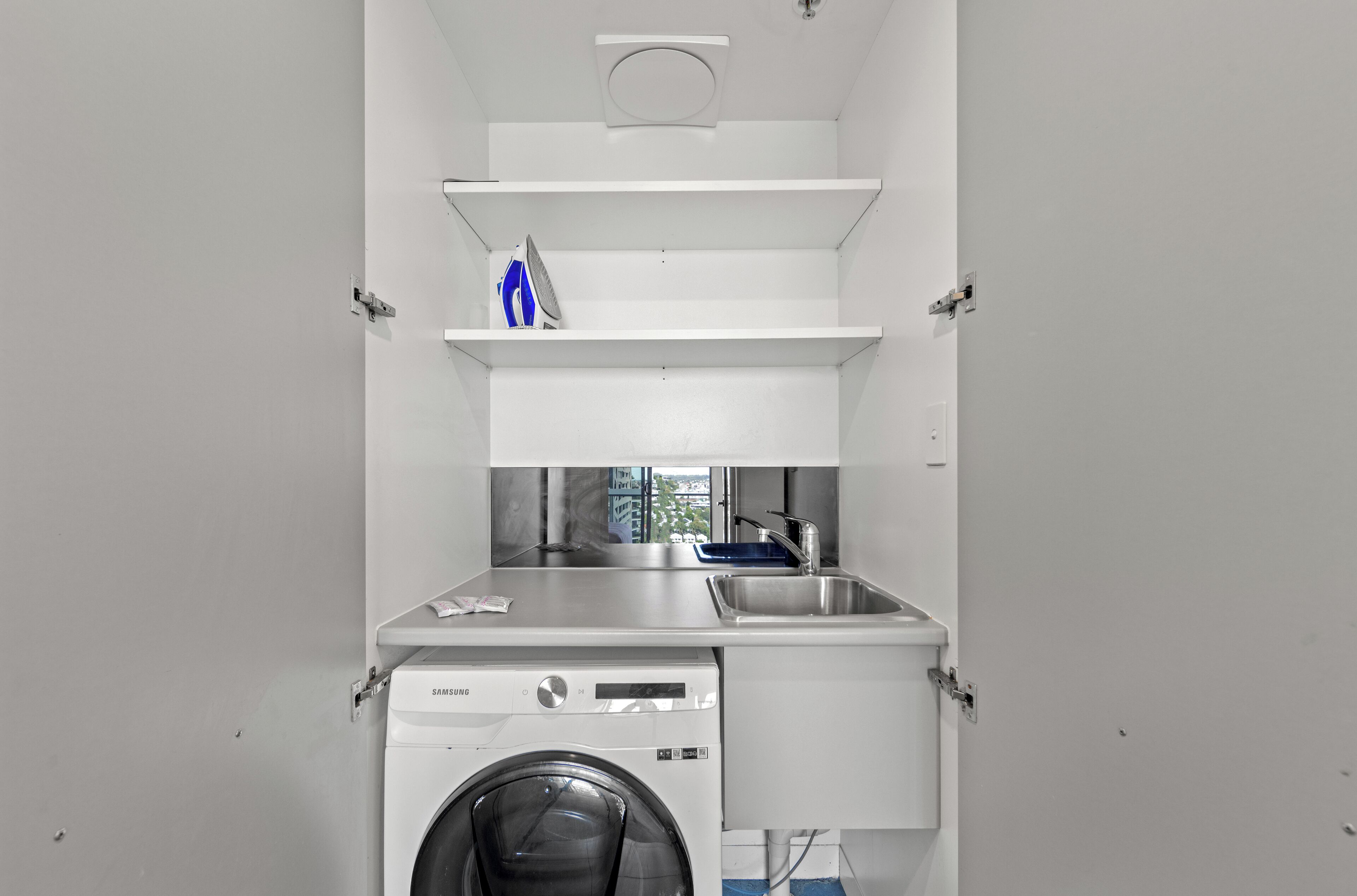 A compact laundry room with a washing machine, a sink, and a drying rack.