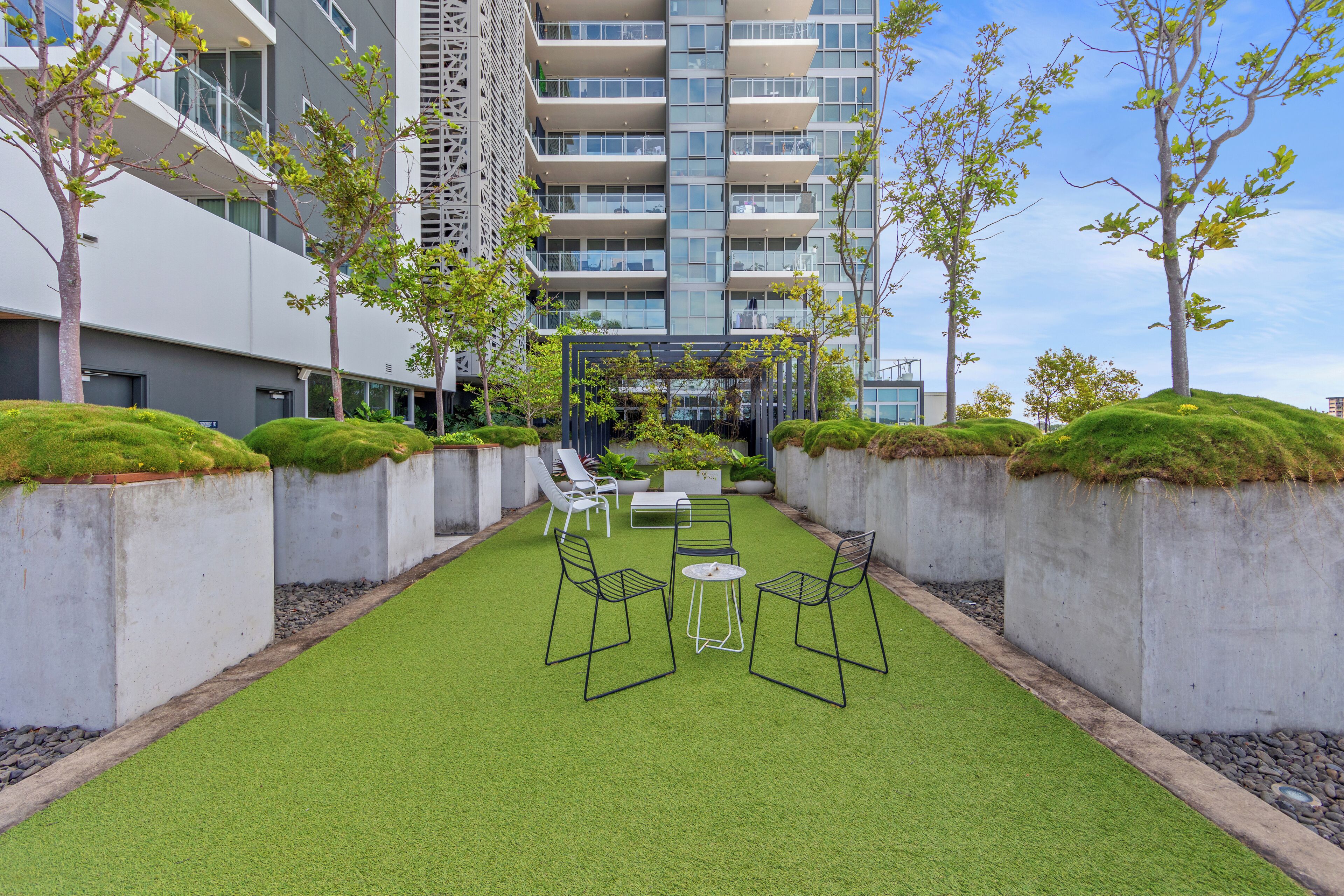 A courtyard with artificial grass, seating, and a view of a high-rise building.