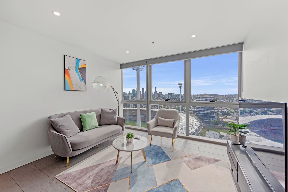 A modern living room with a city view, a sofa, armchairs, a coffee table, and a large window.