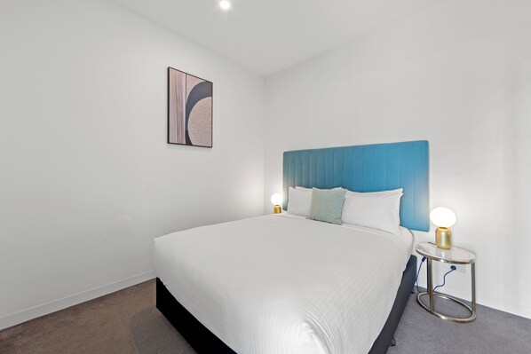 Une chambre d’hôtel moderne avec un grand lit, une tête de lit bleue et une table de chevet avec une lampe.