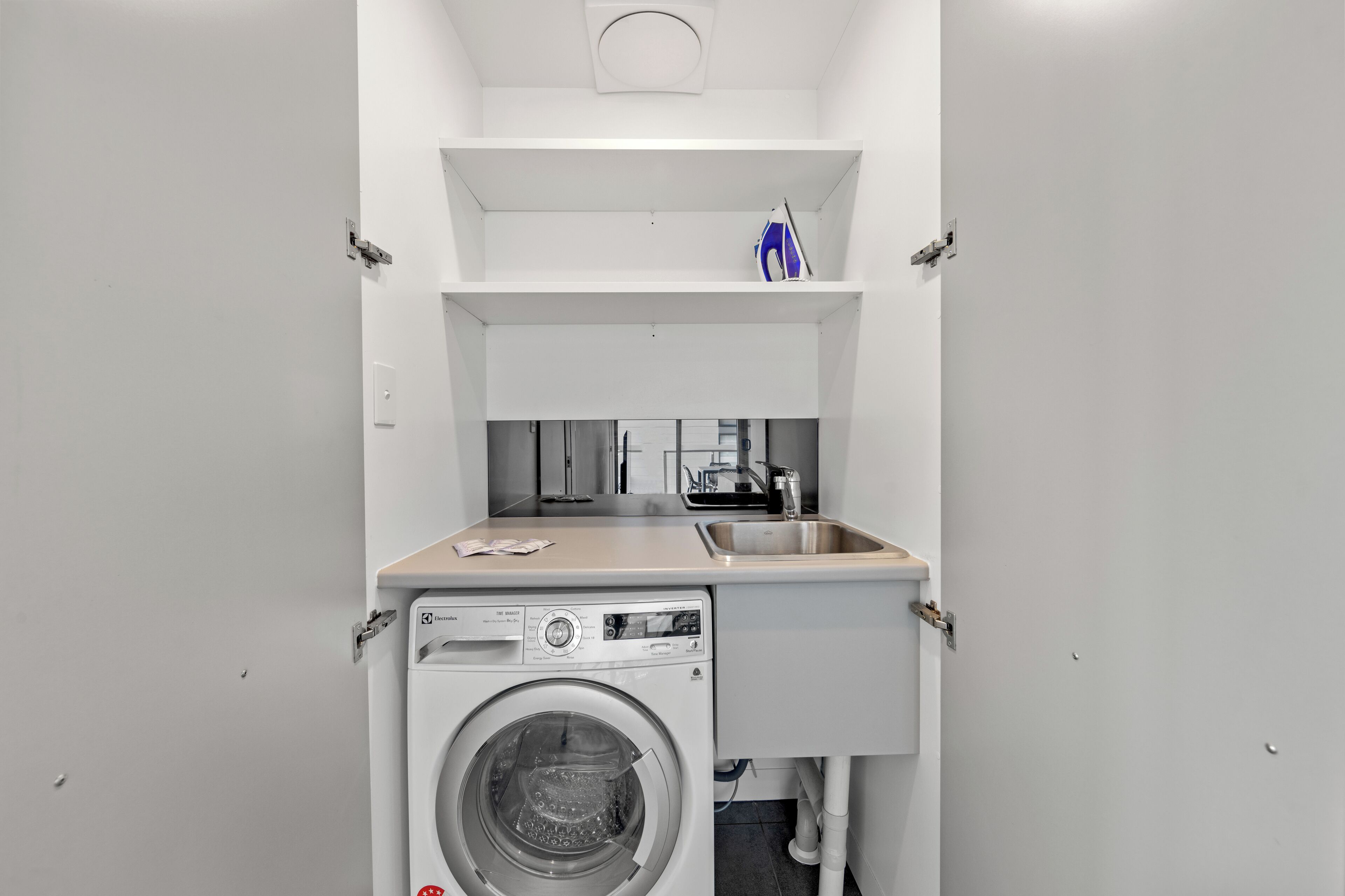 Un área de lavandería compacta con lavadora, un lavamanos y un estante pequeño encima de la máquina.