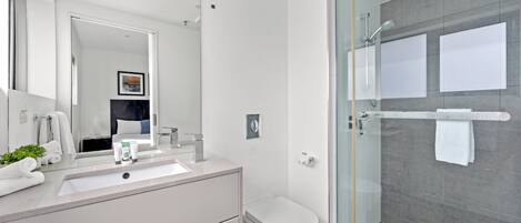 A modern bathroom with a glass shower enclosure, a white sink, and a toilet.
