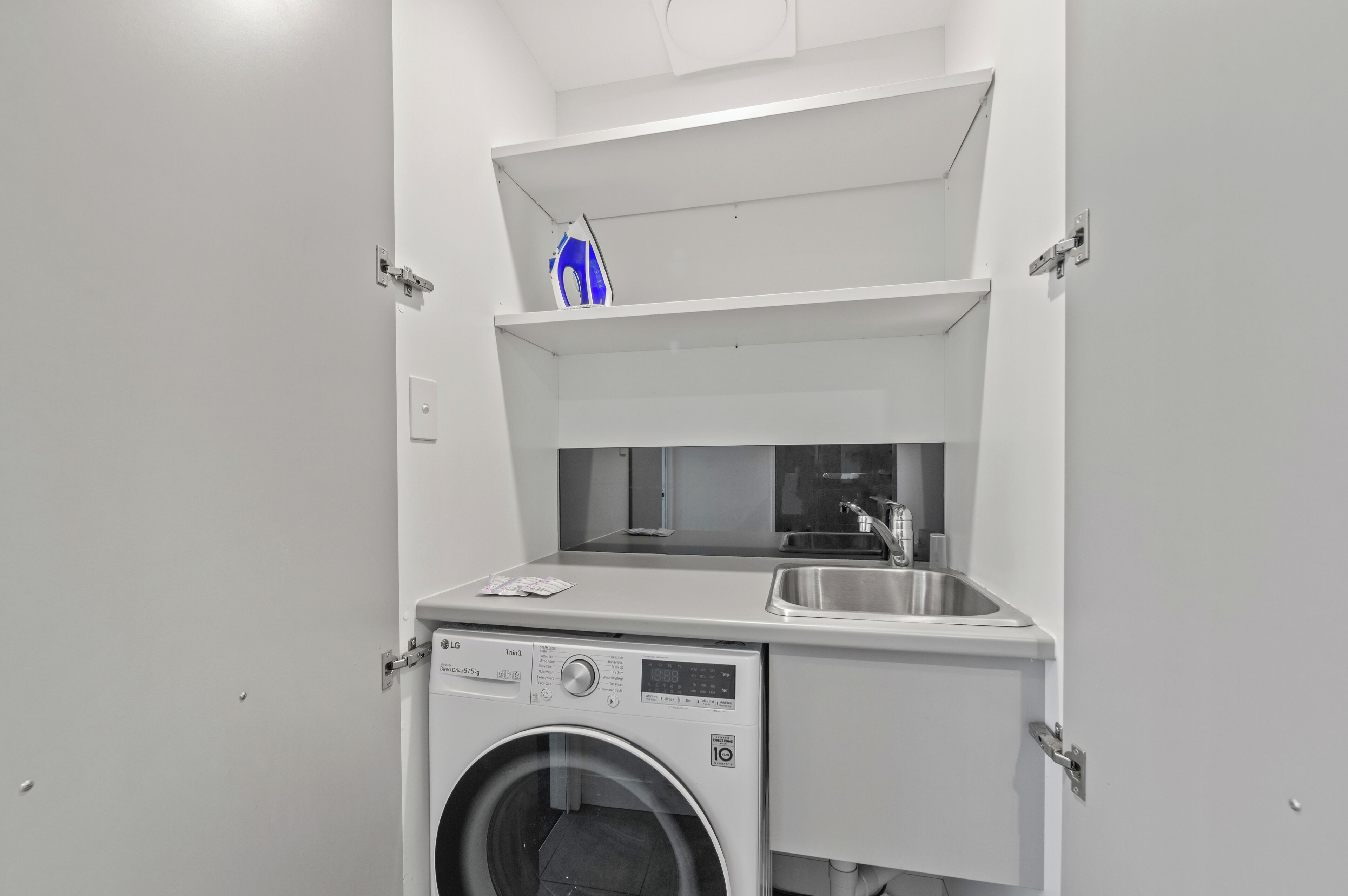 A compact laundry area with a washing machine, a sink, and a shelf above the machine.