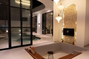 A modern interior with a pool, a flat-screen TV mounted on a textured wall, and a seating area with cushions. - Azure Luxe Private Pool Villa, 6min PererenanBeach (Pererenan)