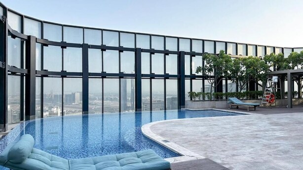 A rooftop infinity pool with a curved glass wall, lounge chairs, and a view of the cityscape.