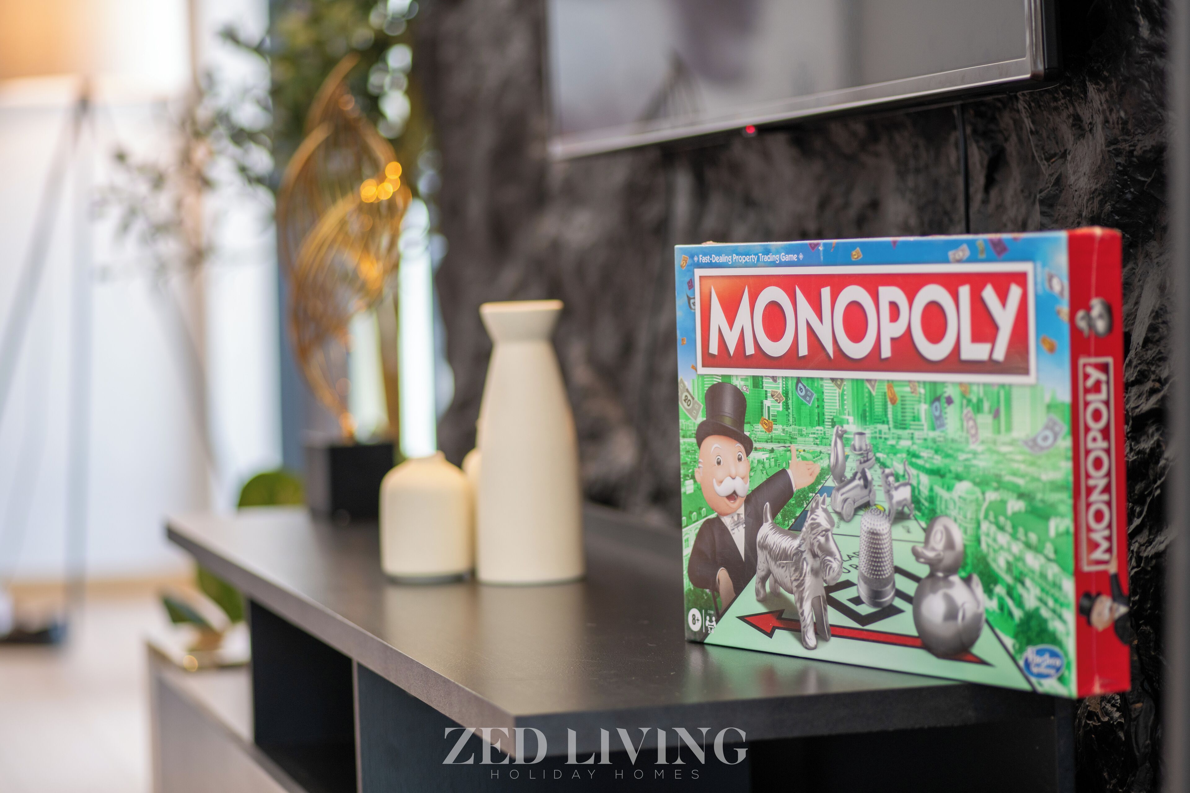 Caja de un juego de Monopoly sobre una superficie negra, con un televisor al fondo.