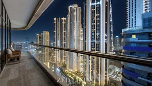 A high-rise balcony with a city view, modern furniture, and illuminated buildings.