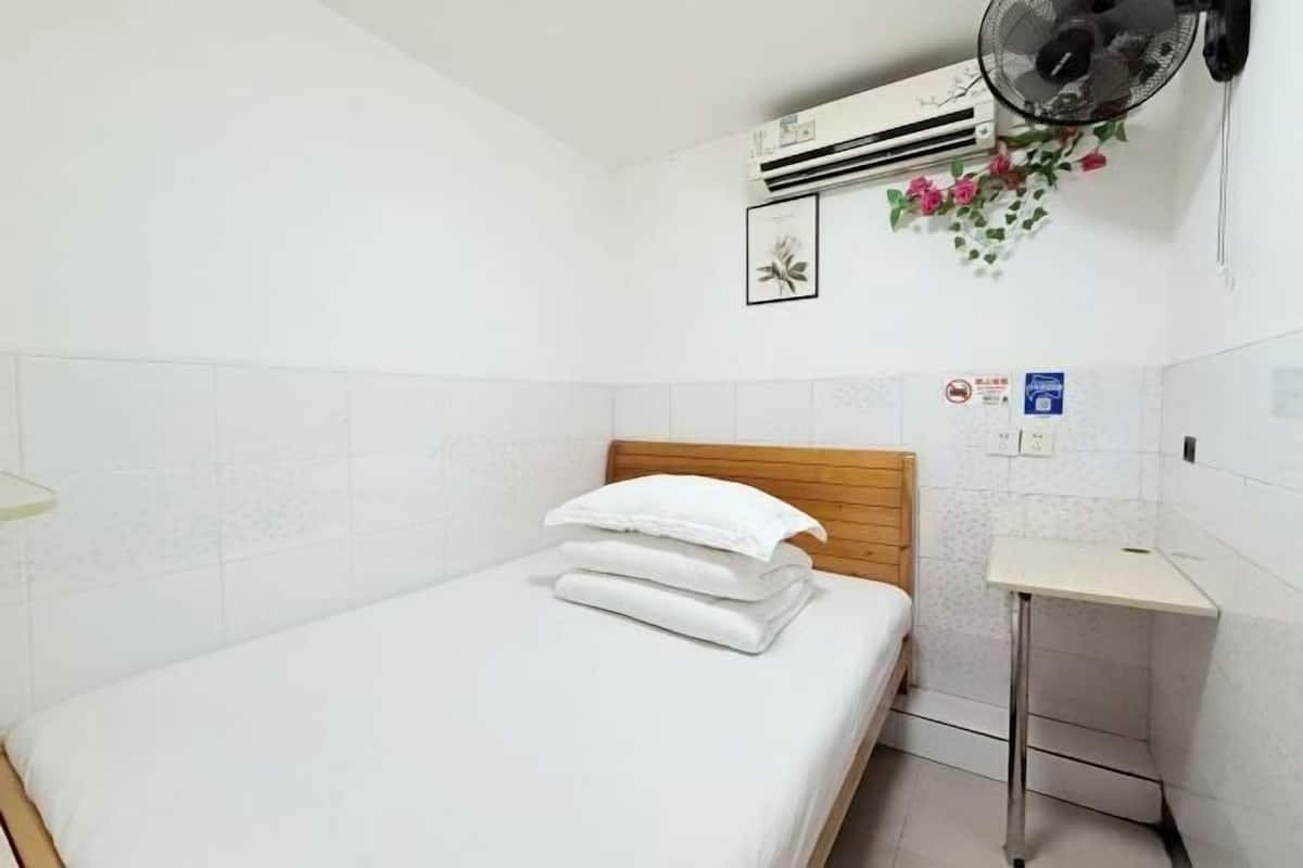 Une chambre d’hôtel comprenant un lit, une petite table de chevet, un appareil de climatisation, un ventilateur fixé au mur et un panneau d’information fixé au mur.
