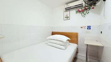 A hotel room with a bed, a small bedside table, an air conditioning unit, a wall-mounted fan, and a wall-mounted sign.