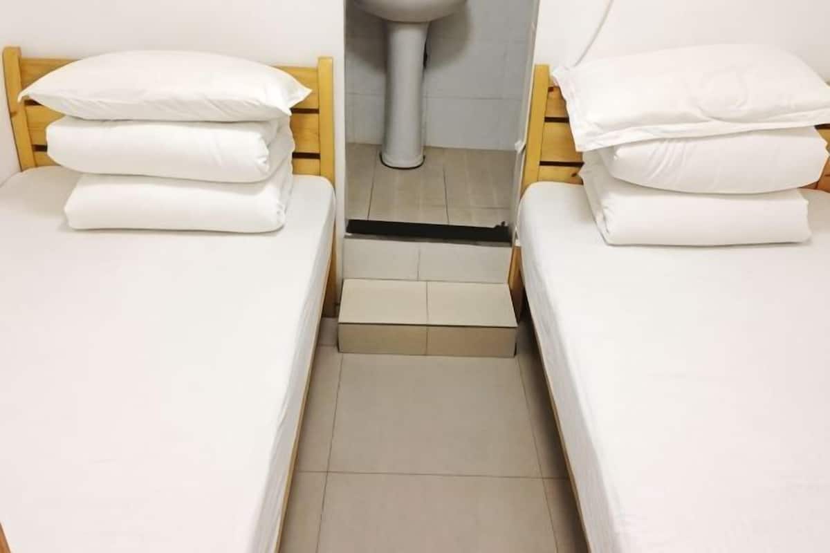 Une petite chambre propre, avec deux lits simples, une salle de bain commune et un aménagement simple et fonctionnel.