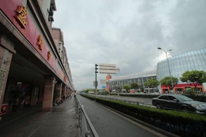 A street with a pedestrian walkway, a modern building with a glass facade, and a traditional building with red signage. - Zhenghong Hostel (Shanghai)