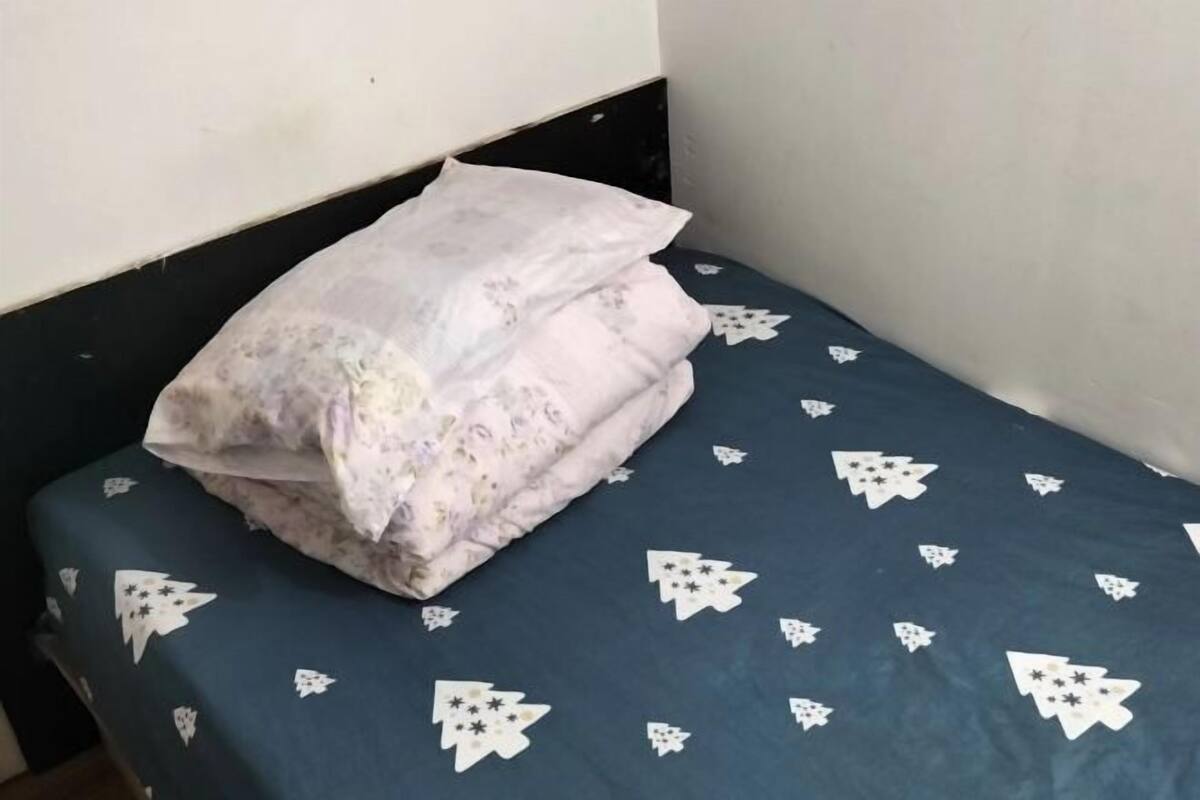 Un lit avec un drap bleu orné de motifs d’arbres blancs, un oreiller blanc et une tête de lit sombre.