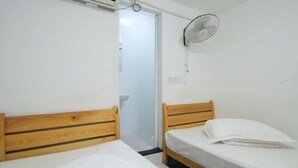 Una habitación pequeña y limpia con dos camas de madera, una pared blanca y un ventilador de techo.