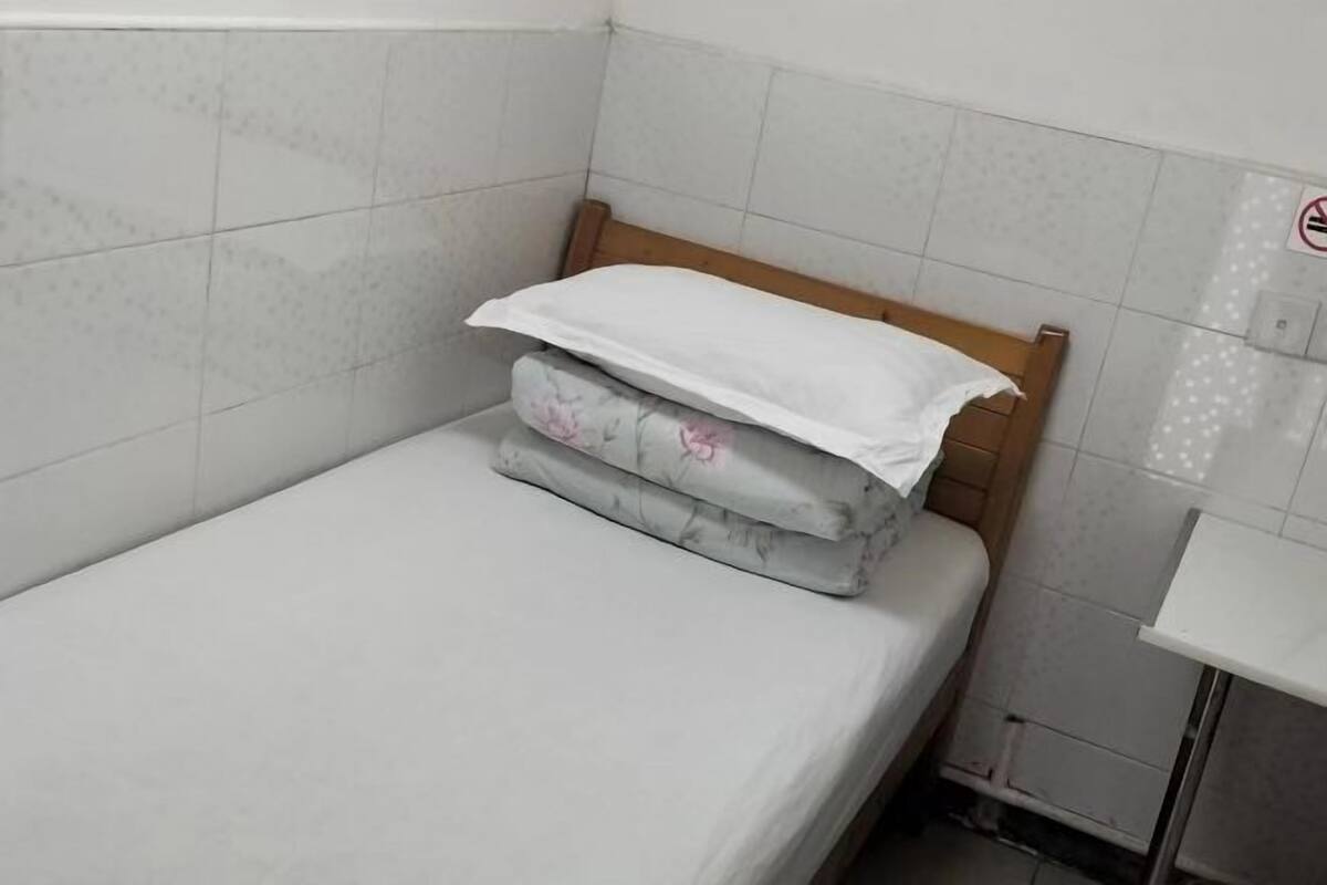 Une petite chambre avec un lit simple, une tête de lit en bois, un matelas blanc et un oreiller à motifs floraux.