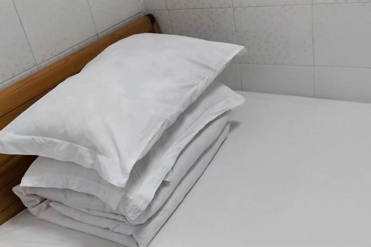 Une pile de coussins blancs, soigneusement rangés, sur un lit dans une pièce dont les murs sont recouverts de carreaux.