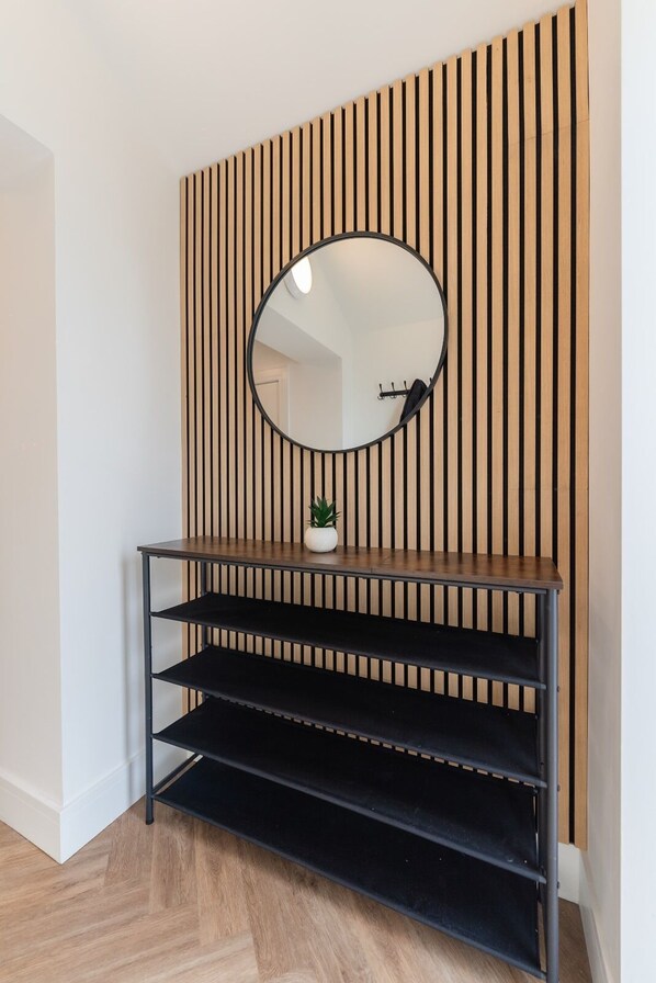 A wooden slat wall with a round mirror above a black metal console table with shelves. - Luxury 8 Bed Home Manchester (Manchester)