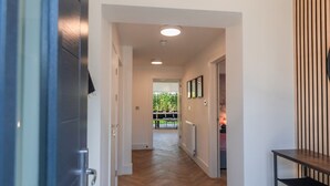 A modern hallway with wooden flooring, recessed ceiling lights, and a view into a dining area. - Luxury 8 Bed Home Manchester (Manchester)